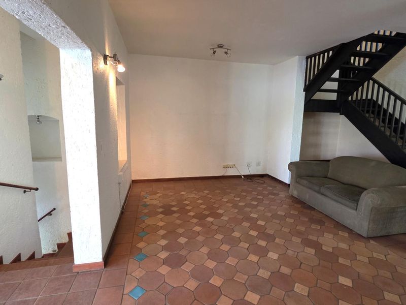 Spacious living area featuring terracotta tile flooring, a built-in staircase with wooden railings, and textured wall finishes.