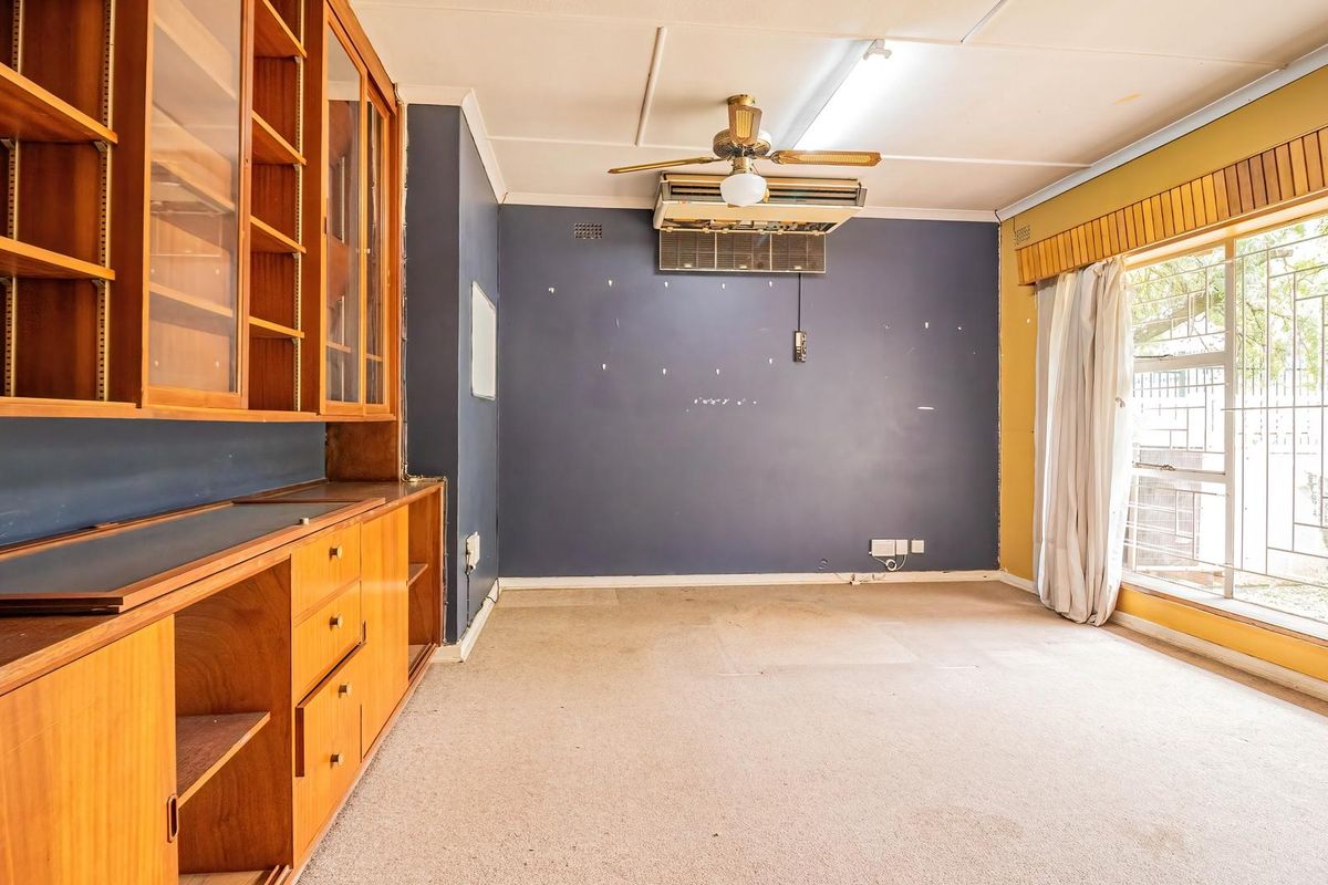 Spacious living area featuring built-in wooden cabinetry, a ceiling fan, and wall-mounted air conditioning, offering a blank canvas for renovation.