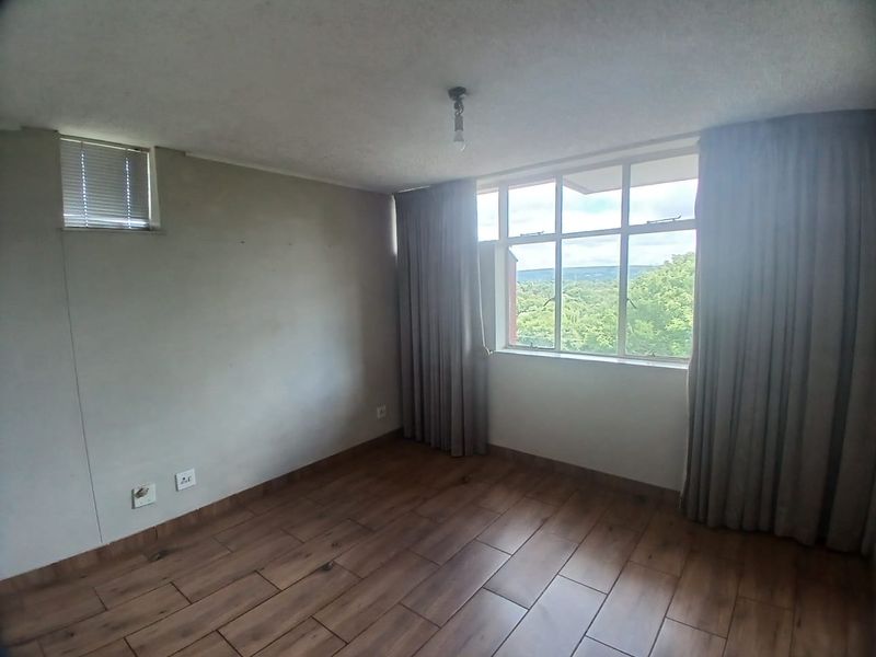 An empty bedroom featuring wood-look tile flooring, large windows with natural light, and neutral wall finishes, ready for personalization.