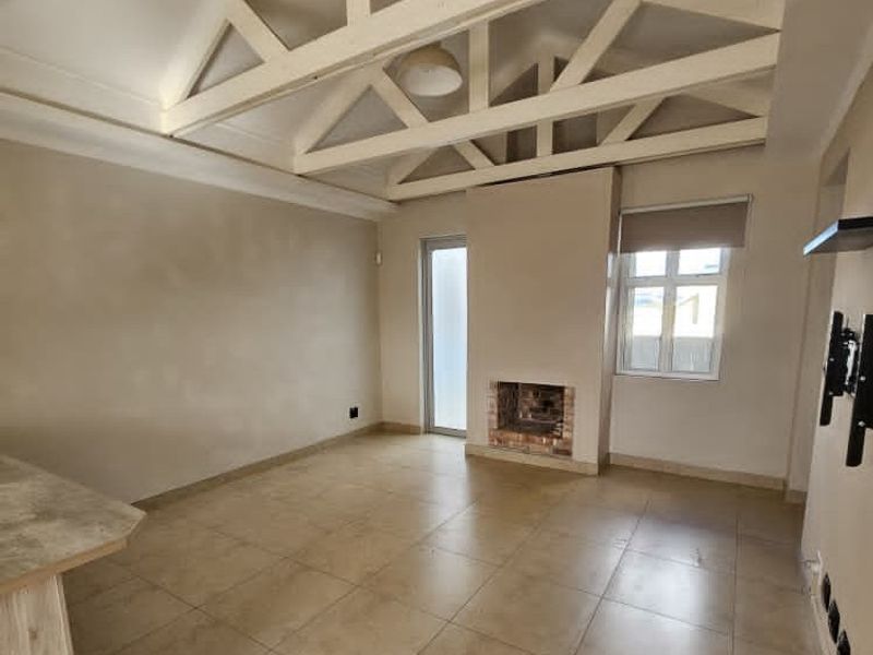 Spacious living area featuring high vaulted ceilings with exposed timber trusses, tiled flooring, and a built-in fireplace.