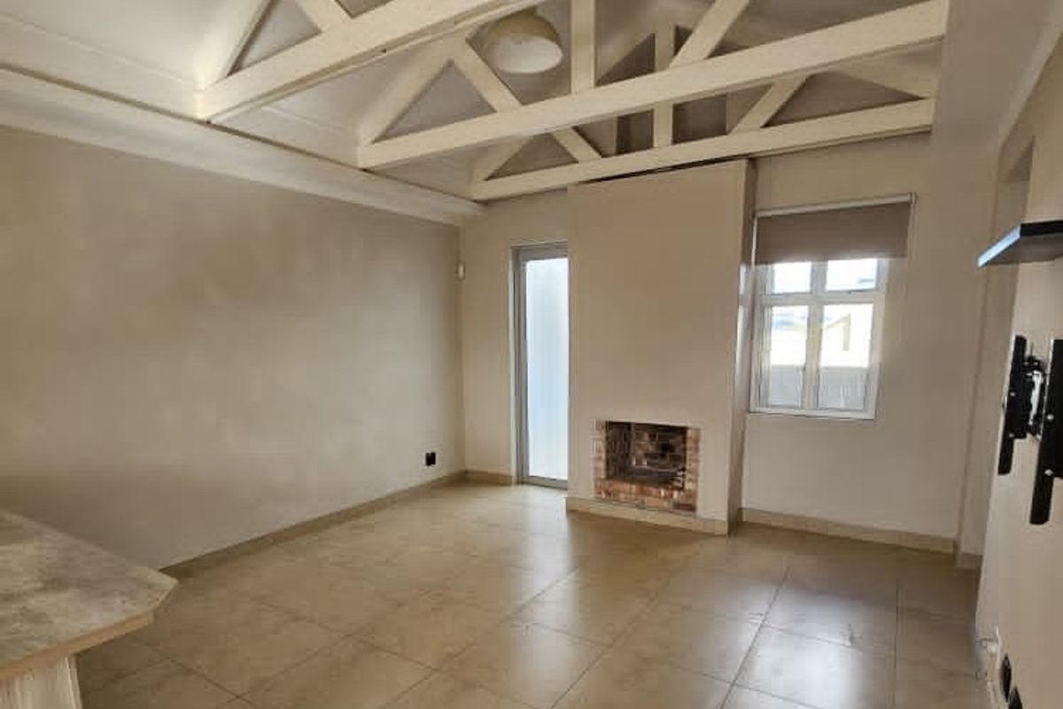 Spacious living area featuring high vaulted ceilings with exposed timber trusses, tiled flooring, and a built-in fireplace.