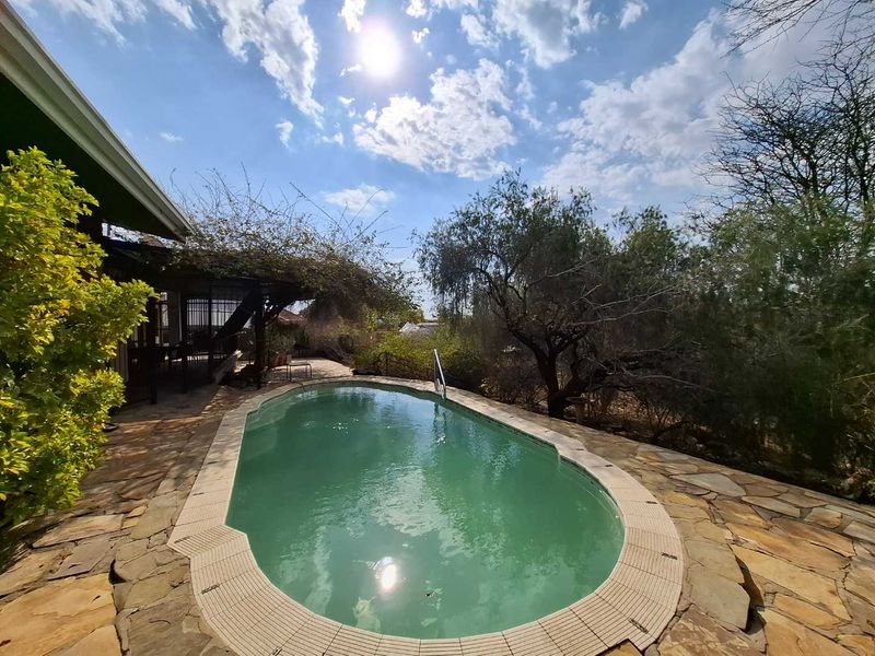 Outdoor pool area featuring stone paving and a covered patio space, set within a landscaped garden environment.
