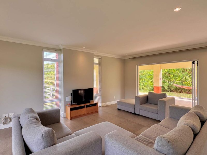 Spacious living room featuring tiled flooring, recessed downlights, and large sliding glass doors that provide seamless access to the outdoor patio area.