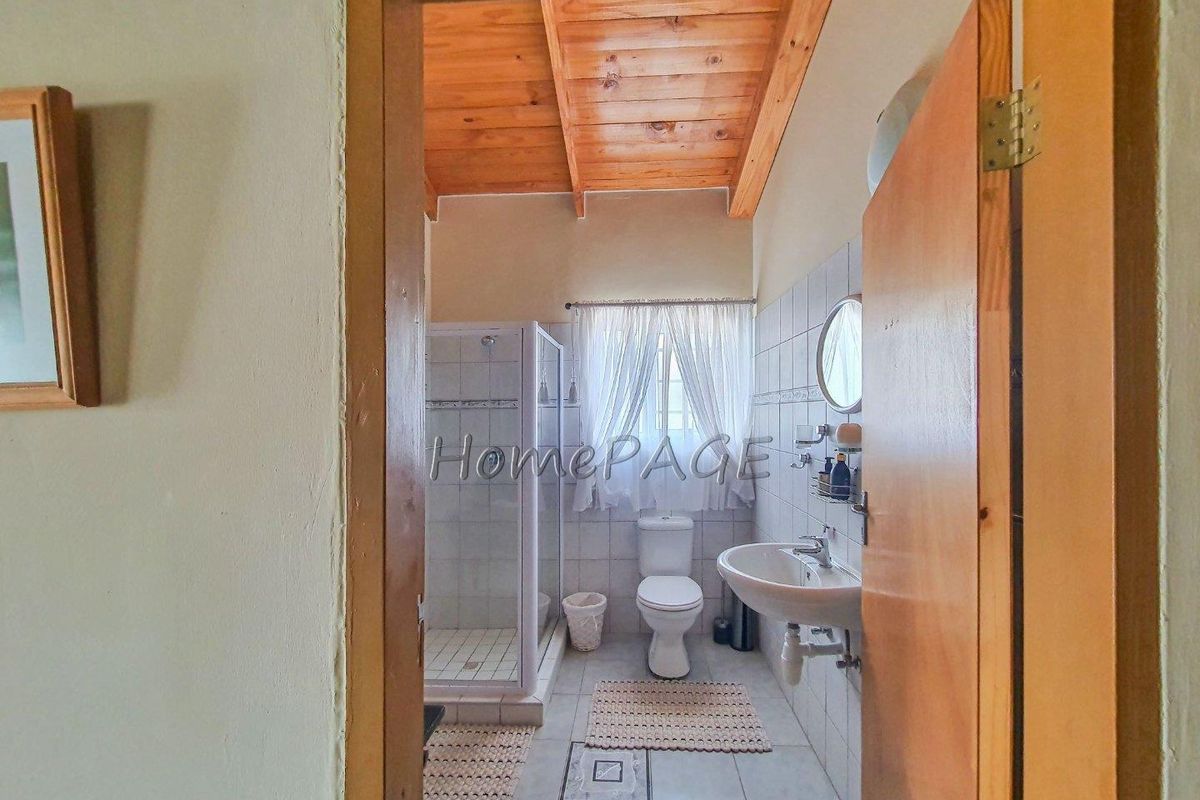 A functional bathroom featuring a shower enclosure, pedestal basin, and toilet, highlighted by a vaulted timber-clad ceiling.
