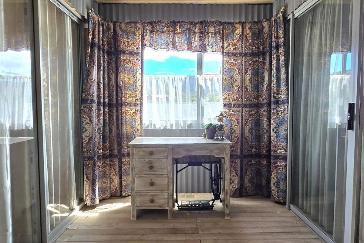 A sun-filled room featuring large sliding glass doors, timber flooring, and a window with views, currently utilized as a workspace.