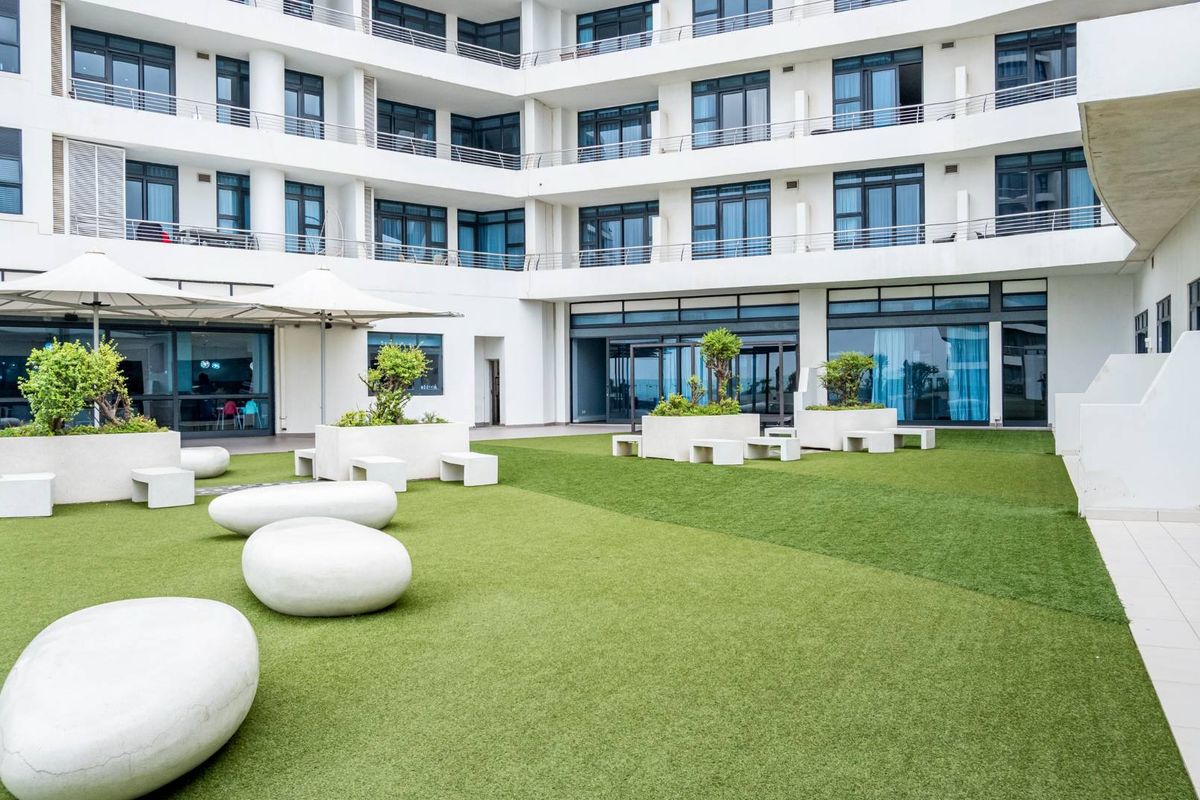A well-maintained communal courtyard area featuring artificial turf, built-in concrete planters, and integrated seating, set against a modern apartment building facade.