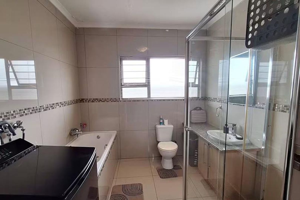 A functional bathroom featuring a bathtub, separate glass shower enclosure, vanity with basin, and toilet, finished with neutral wall and floor tiles.