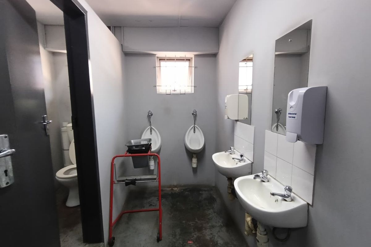 Functional industrial-style communal bathroom featuring dual urinals, wall-mounted basins, and a separate toilet cubicle with basic finishes.
