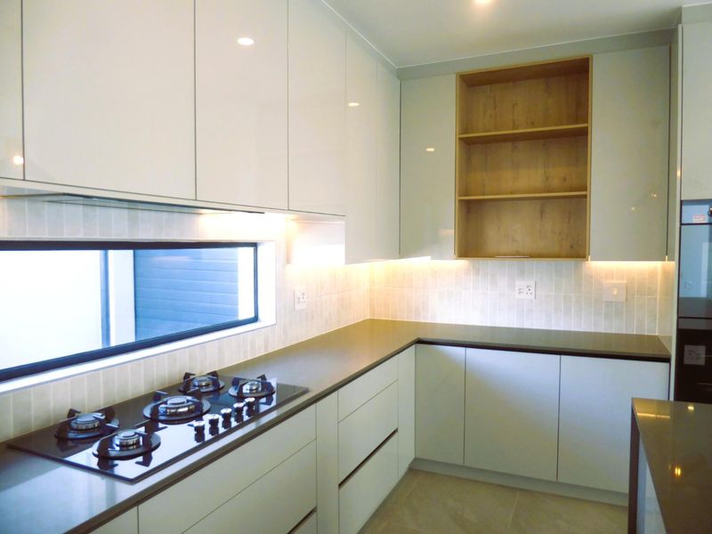 Modern kitchen featuring sleek gloss cabinetry, stone benchtops, integrated gas cooktop, and stylish under-cabinet lighting with open shelving.