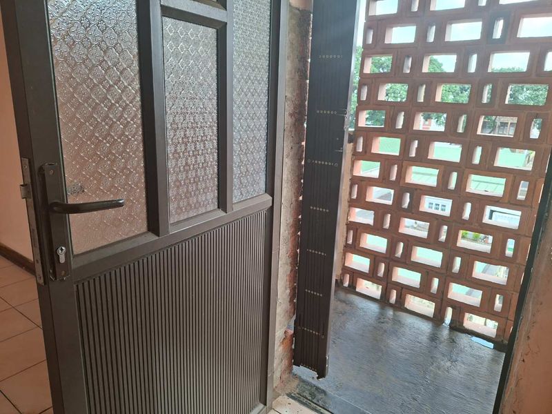 A balcony area featuring a decorative breeze block screen wall, tiled flooring, and a metal security door with textured glass panels.