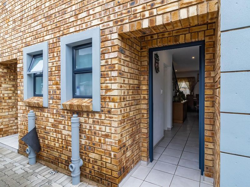 Front entrance of the townhouse featuring face brick exterior, tiled flooring, and casement windows leading into the main living area.