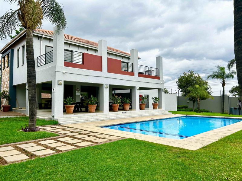 A well-maintained outdoor pool area featuring a large swimming pool, a spacious covered patio, and an upper-level balcony with modern architectural finishes.