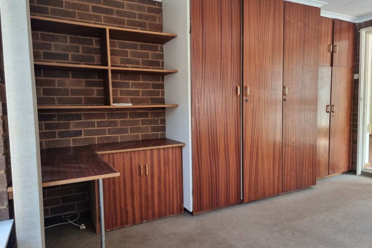 A bedroom featuring built-in wooden wardrobes and a matching integrated desk unit against a brick feature wall.