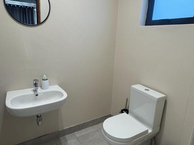 A clean and modern guest bathroom featuring a wall-mounted basin, contemporary toilet, and neutral floor tiling.