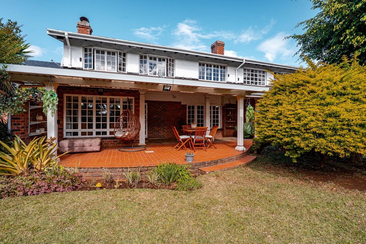 A spacious rear exterior view of the townhouse featuring a covered terracotta tiled patio, brick facade, and established garden area.