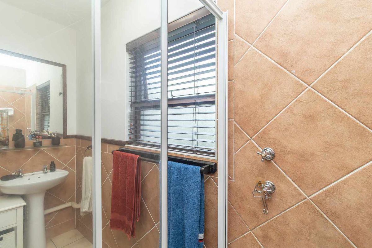 A functional bathroom featuring a pedestal sink, shower enclosure with glass door, and tiled walls with a window for natural light.