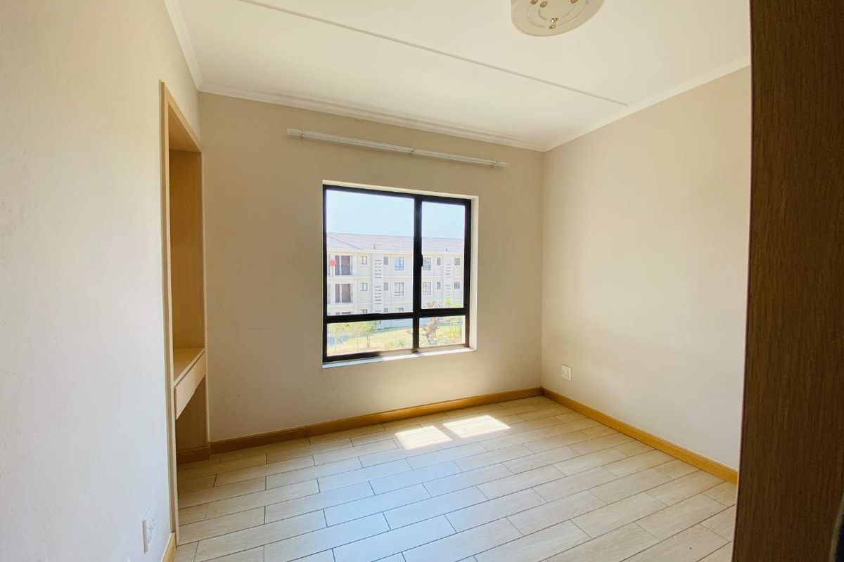 A bright, empty bedroom featuring neutral wall finishes, tiled flooring, and a built-in recessed shelving unit.