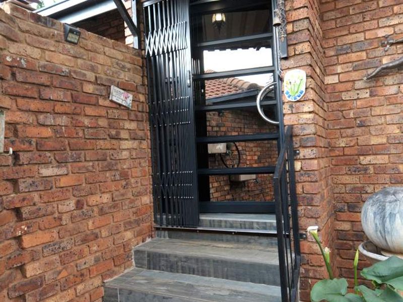 Entrance area featuring a tiled staircase, exposed brick walls, and a secure metal gate with an overhead awning.