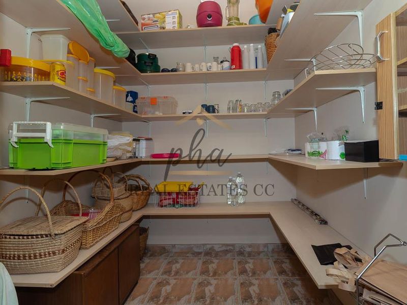 A functional walk-in pantry or scullery area featuring extensive built-in shelving and durable tiled flooring for organized storage.