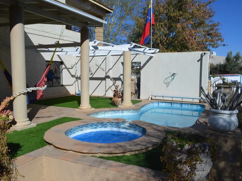Outdoor pool area featuring a built-in spa, covered patio with concrete columns, and artificial turf landscaping.