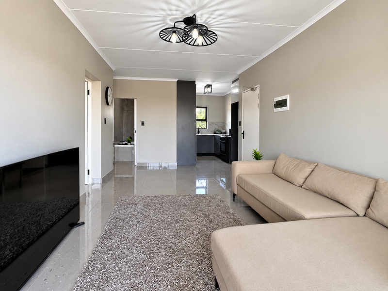 Spacious open-plan living area featuring polished tiled floors, modern neutral walls, and a sleek, contemporary kitchen with integrated appliances.