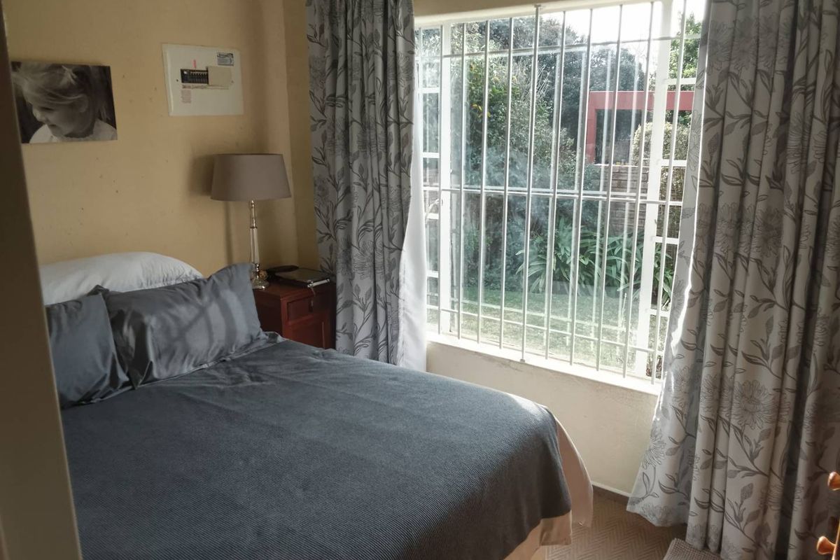 A bedroom featuring a window with security bars, providing natural light and a view of the garden area.