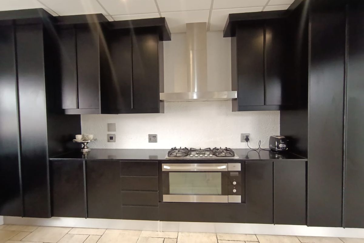 Modern kitchen featuring sleek black cabinetry, stainless steel built-in oven, gas hob, extractor fan, and durable tiled flooring.