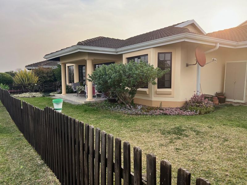 Rear view of a townhouse featuring a covered patio, landscaped garden, and a wooden picket fence.