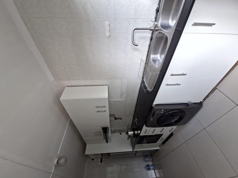 A compact kitchen featuring built-in cabinetry, a double stainless steel sink, and tiled finishes, currently showing signs of incomplete wall tiling.