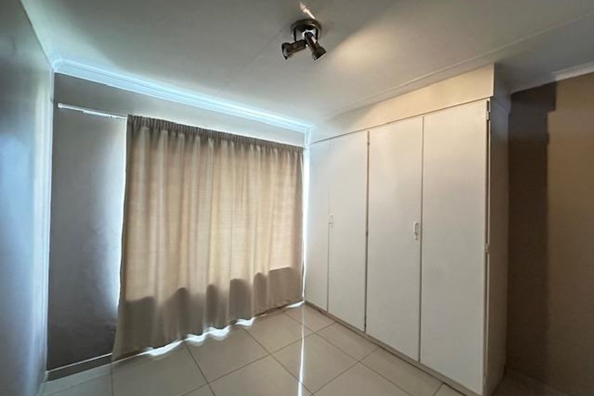 A bedroom featuring built-in cupboards, tiled flooring, and a ceiling-mounted spotlight fixture.