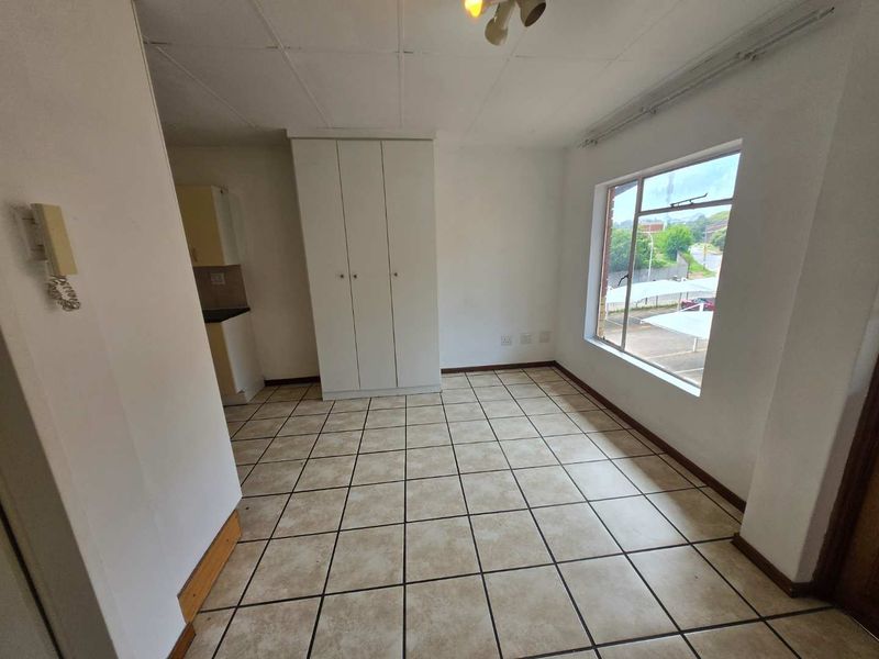 An open-plan living area featuring tiled flooring, a built-in wardrobe, and an intercom system, with a view through the window.
