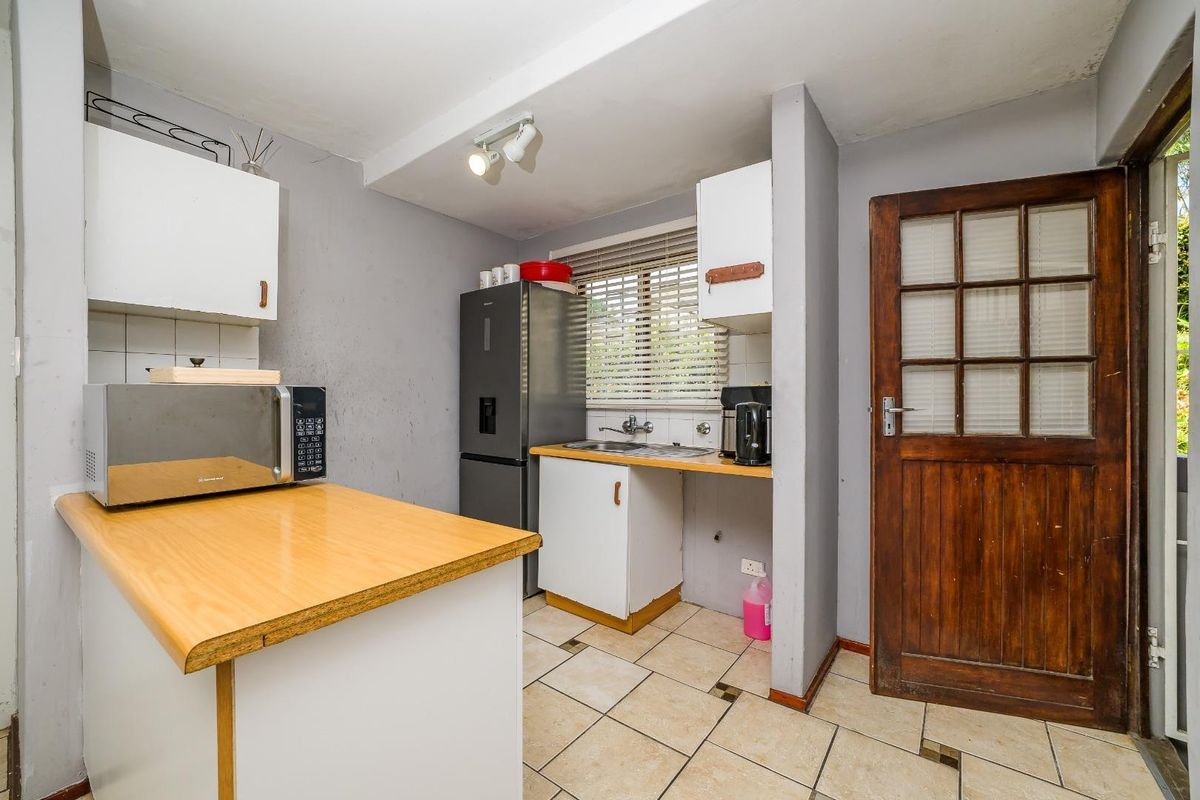 A compact kitchen featuring laminate countertops, tiled flooring, and a timber door leading to the exterior, offering potential for cosmetic updates.