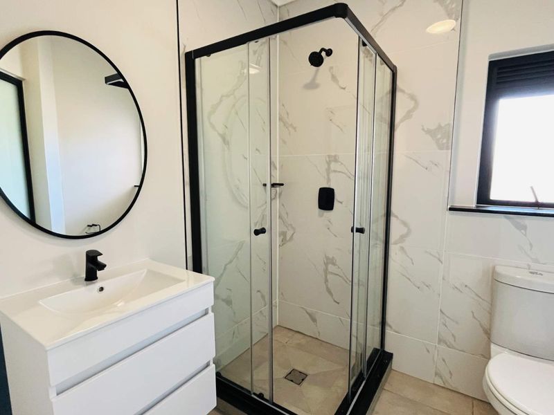 Modern bathroom featuring a sleek vanity, glass-enclosed shower, and contemporary toilet with marble-look wall tiles and black fixtures.