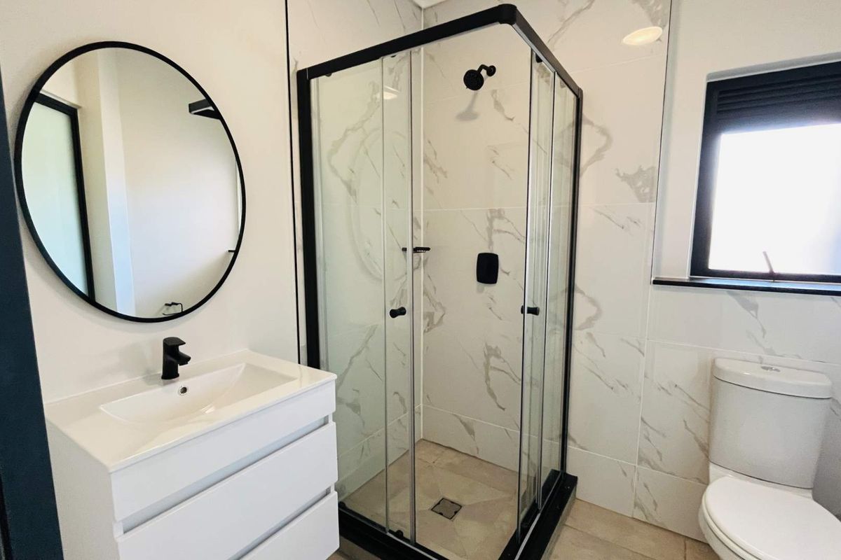 Modern bathroom featuring a sleek vanity, glass-enclosed shower, and contemporary toilet with marble-look wall tiles and black fixtures.