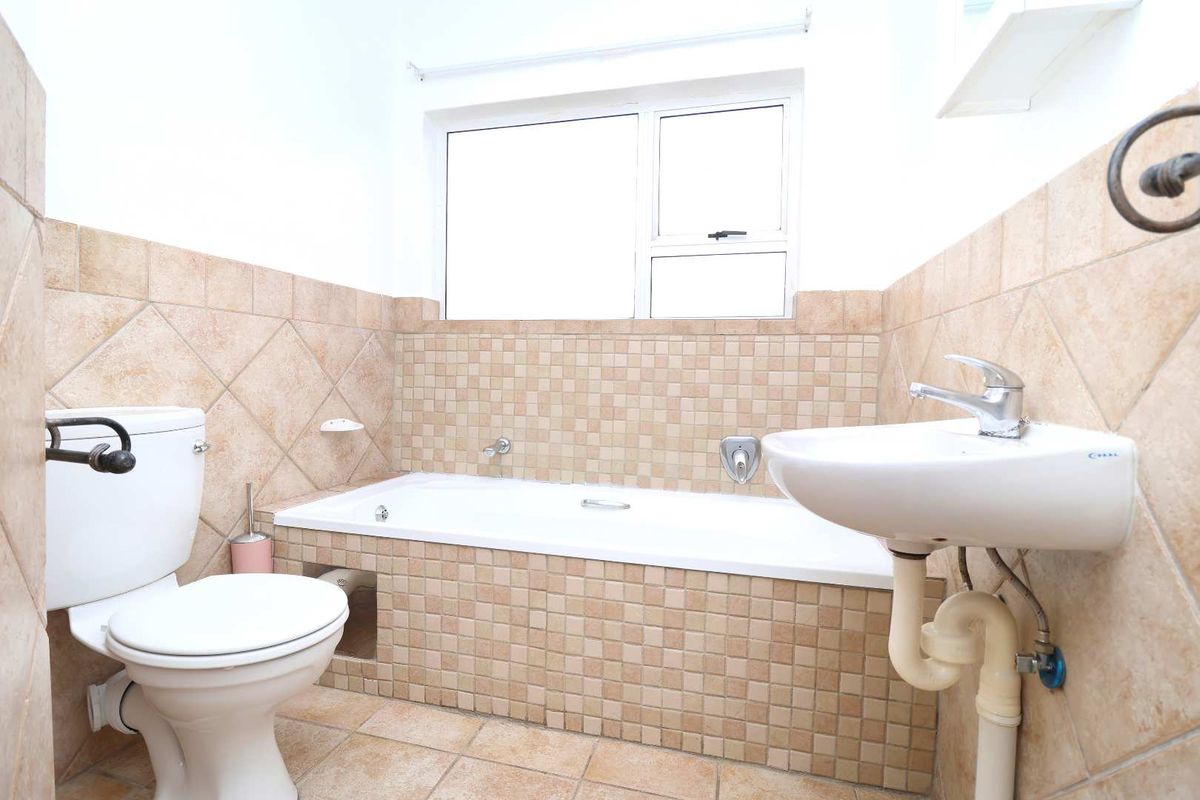 A functional bathroom featuring a built-in bathtub, pedestal washbasin, and toilet, finished with neutral ceramic wall and floor tiling.