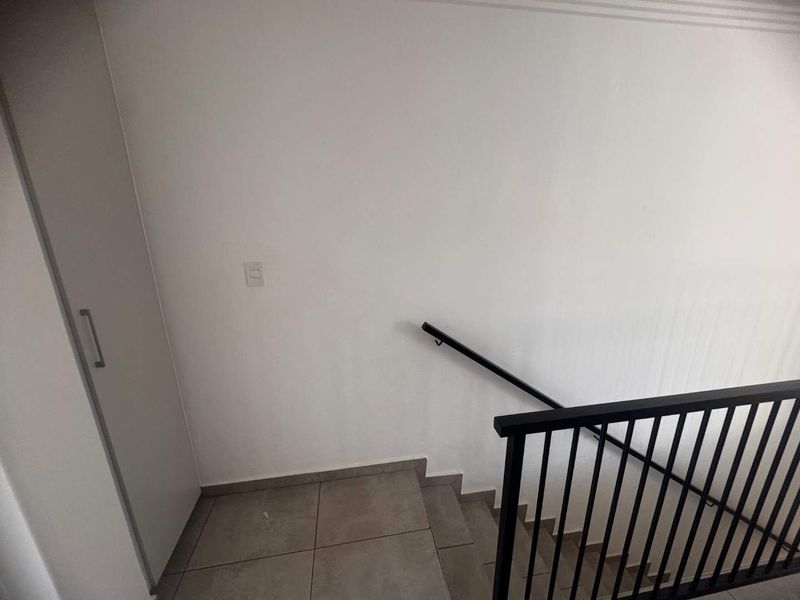 A clean, minimalist hallway featuring a staircase with a modern black metal balustrade and neutral tiled flooring.