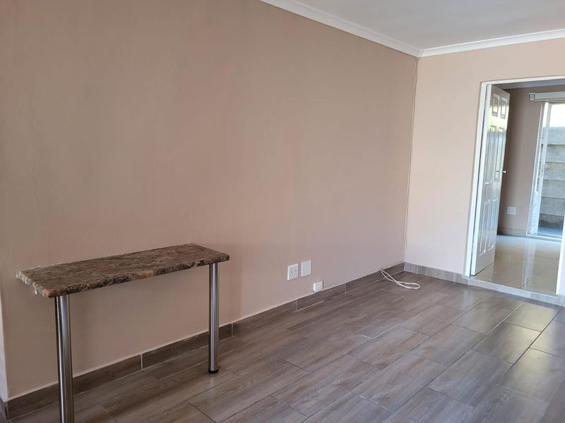 A bright, empty living area featuring neutral wall tones, modern wood-look floor tiles, and coving, providing a clean and versatile space.