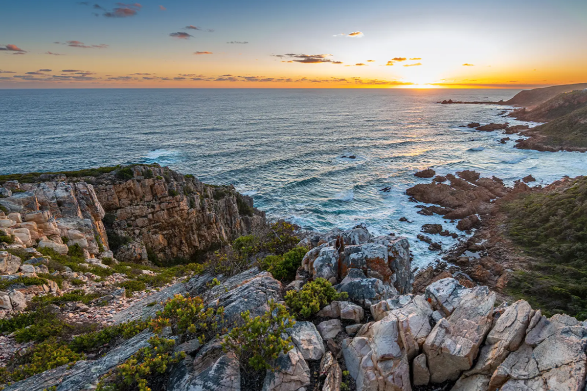 A stunning panoramic view of the rugged coastline, rocky cliffs, and ocean at sunset, showcasing the natural beauty of the vacant land.