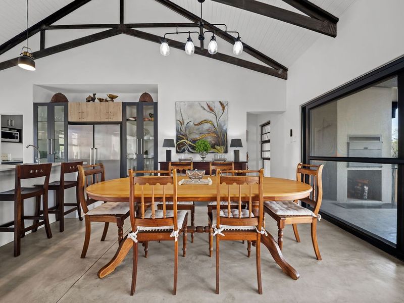 Spacious open-plan living and dining area featuring vaulted ceilings with exposed timber trusses, polished concrete floors, and seamless access to the outdoor patio.