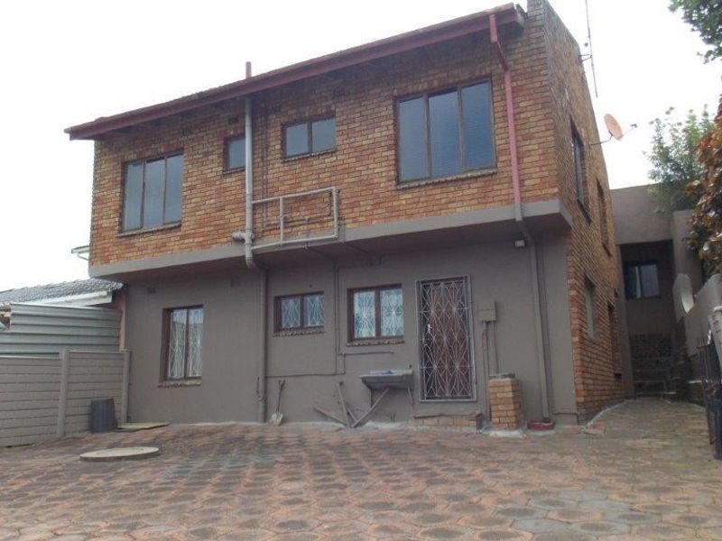 Rear view of a two-story brick house featuring a paved courtyard, security gate, and external wash basin area.