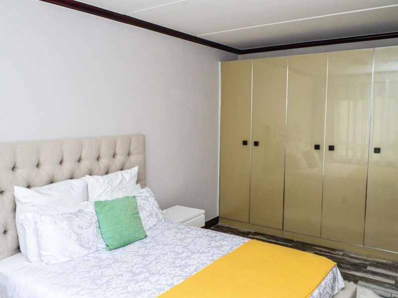 A well-maintained bedroom featuring neutral walls, crown molding, and floor-to-ceiling built-in cupboards with a glossy finish.