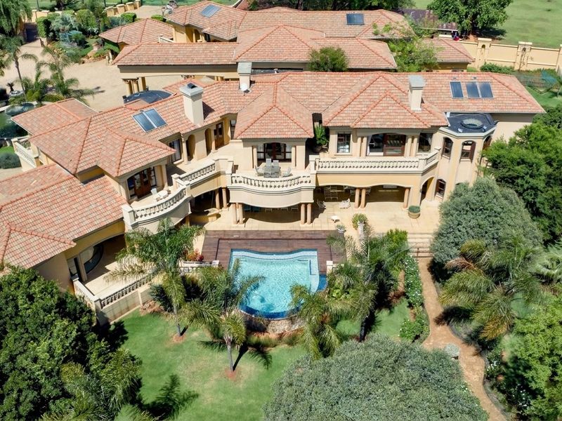Aerial view of a large luxury residence featuring a terracotta tile roof, multiple balconies, a swimming pool with wooden decking, and extensive landscaped grounds.