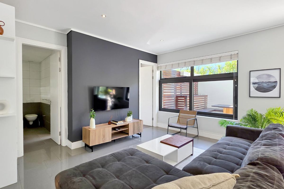 Modern living room featuring a dark grey accent wall, tiled flooring, recessed lighting, and large windows providing natural light and a view of the patio.