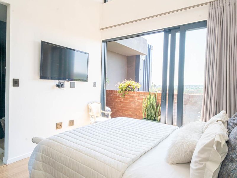Modern bedroom featuring laminate flooring, an en-suite bathroom with a vanity, and large sliding glass doors opening onto a private balcony.
