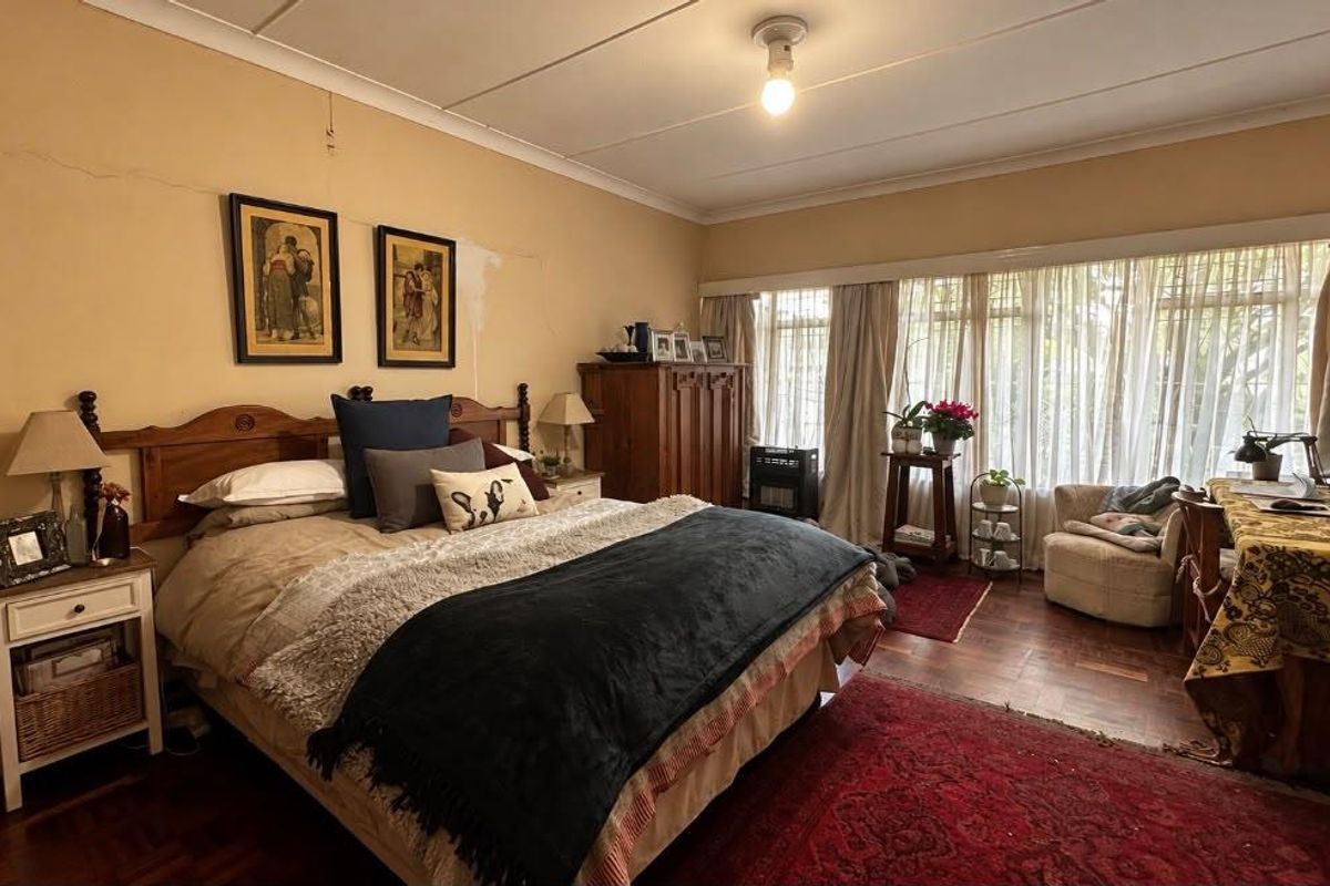 Spacious bedroom featuring parquet flooring and large windows, currently requiring cosmetic attention to the wall finishes.
