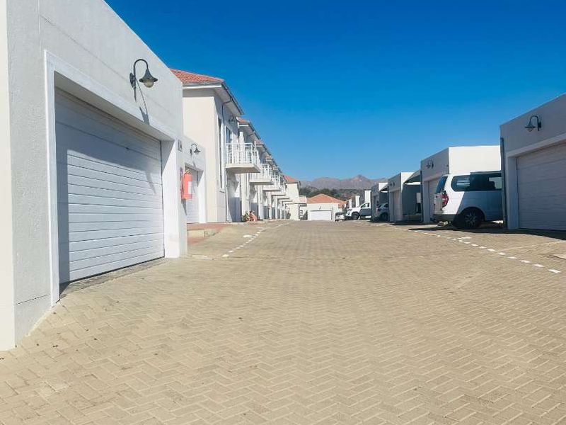 A view of the townhouse complex driveway featuring multiple garage entrances and residential units with balconies under a clear sky.