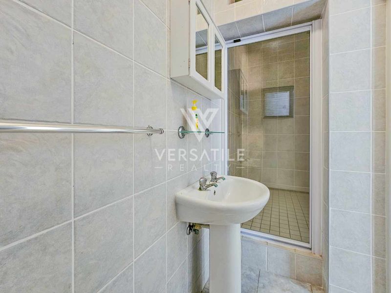 A functional bathroom featuring a pedestal basin, tiled walls, and a separate shower enclosure with a glass door.