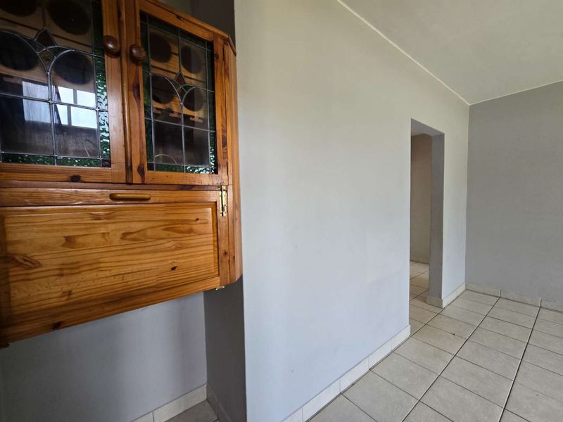 An empty living area featuring neutral grey walls, tiled flooring, and a built-in wooden wall cabinet with leaded glass detailing.