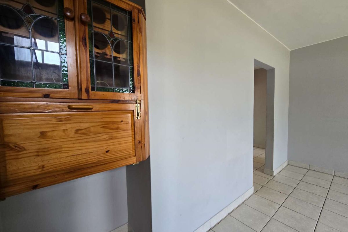 An empty living area featuring neutral grey walls, tiled flooring, and a built-in wooden wall cabinet with leaded glass detailing.