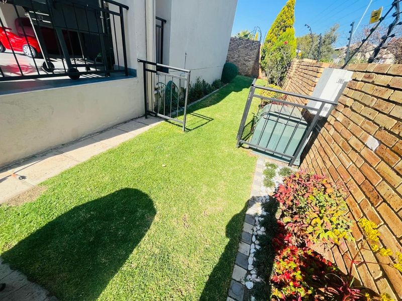A side garden area featuring a manicured lawn, brick boundary wall with electric fencing, and a metal security gate.